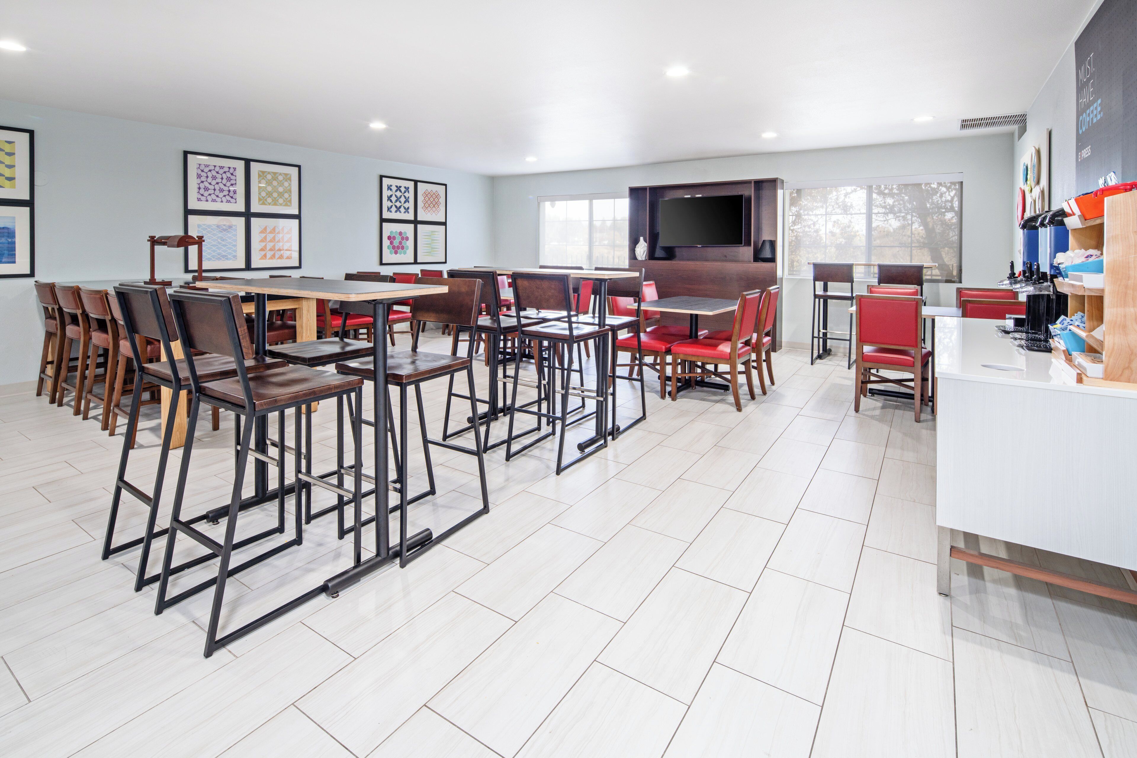 A modern dining area with multiple tables and chairs, a flat-screen TV mounted on the wall, and framed artwork on the walls.