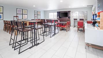 A modern dining area with multiple tables and chairs, a flat-screen TV mounted on the wall, and framed artwork on the walls.