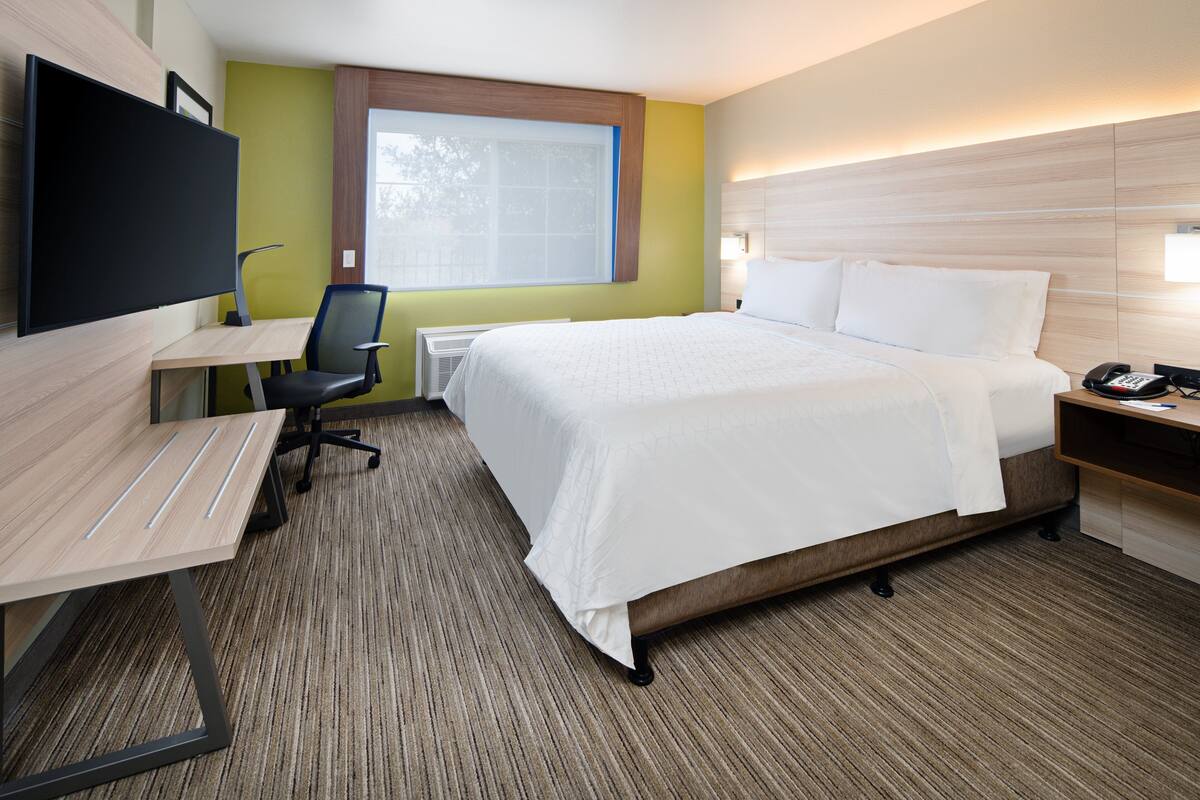 A hotel room with a bed, desk, chair, TV, and bedside table.