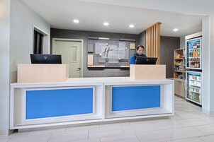 A reception desk with two computer stations, a refrigerator stocked with beverages, and a wall-mounted sign indicating the hotel name.