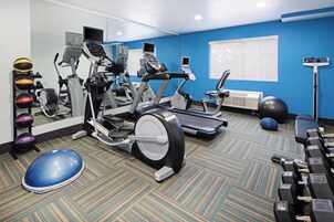 Un gimnasio con diverso equipo de ejercicio, incluyendo cintas de correr, elípticas y pesas libres.