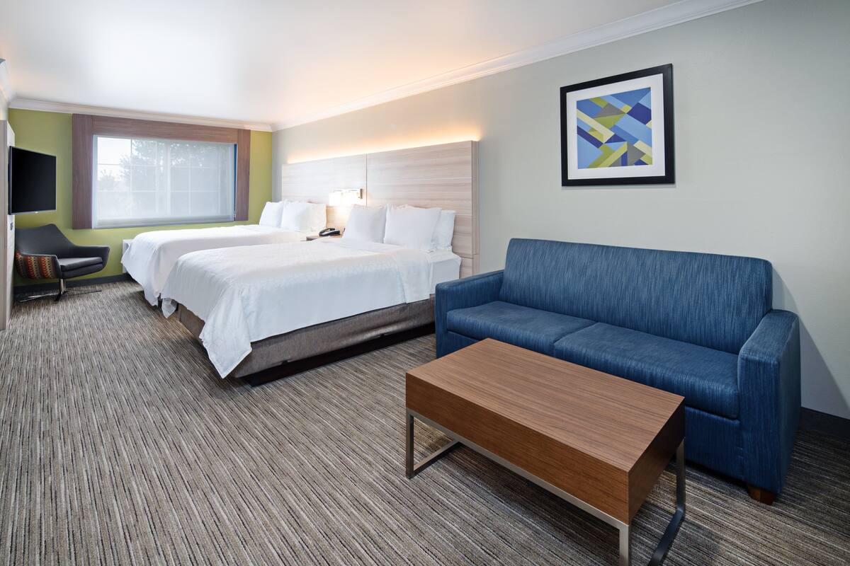 A hotel room with two beds, a blue sofa, a wooden coffee table, a TV, and a framed picture on the wall.