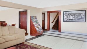 Amplia sala de estar con un sofá color beige, un sillón rojo y una alfombra estampada. Una escalera con barandilla de madera conduce a otro nivel.