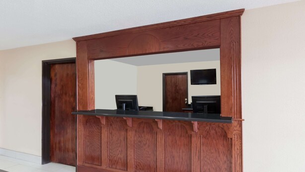 Un mostrador de recepción con estructura de madera y encimera negra, flanqueado por dos puertas y un televisor montado en la pared.