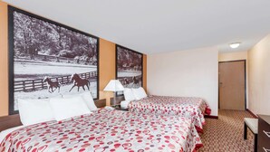 Habitación de hotel con dos camas, una mesita de noche, una lámpara y un cuadro grande con caballos en la pared.