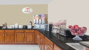 Una cocina con armarios de madera, una encimera negra, una cafetera, un tostador y un bol de manzanas.
