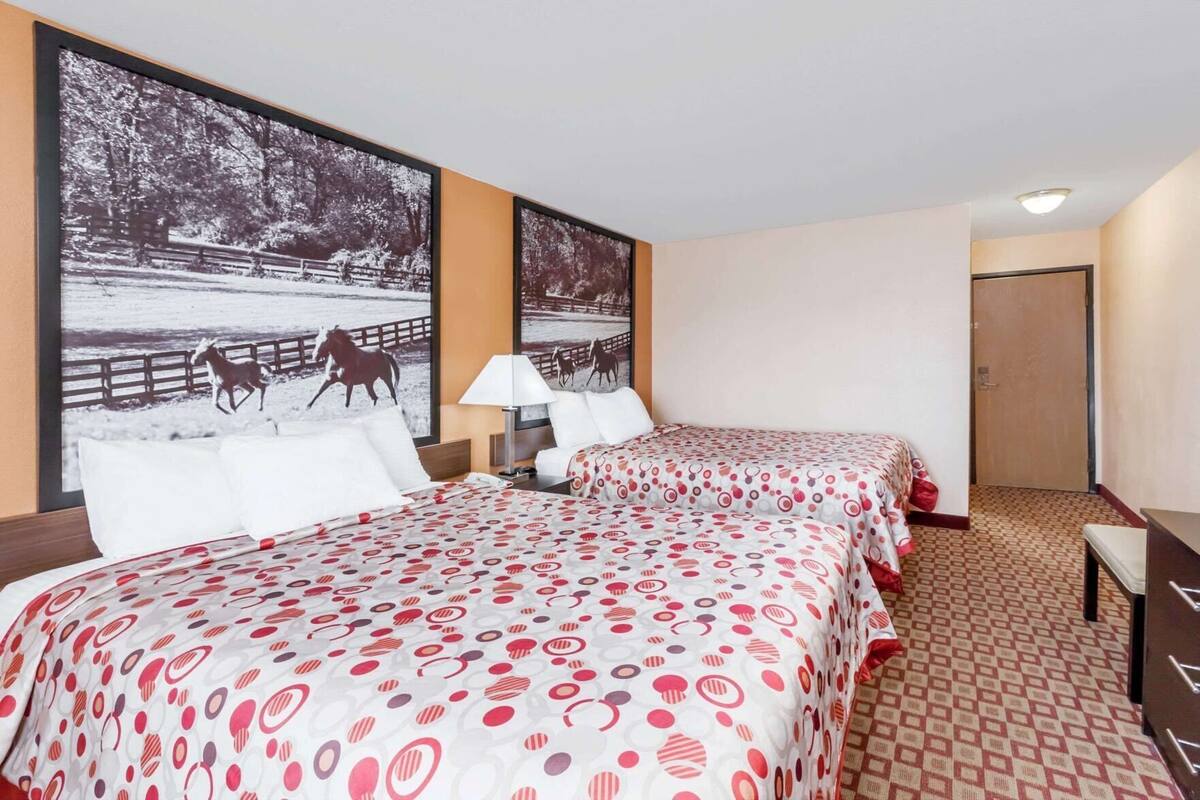 A hotel room with two beds, a nightstand, a lamp, and a large wall-mounted picture of a snowy park scene.