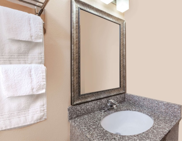 A bathroom with a granite countertop, a white sink, and a mirror with a decorative frame.