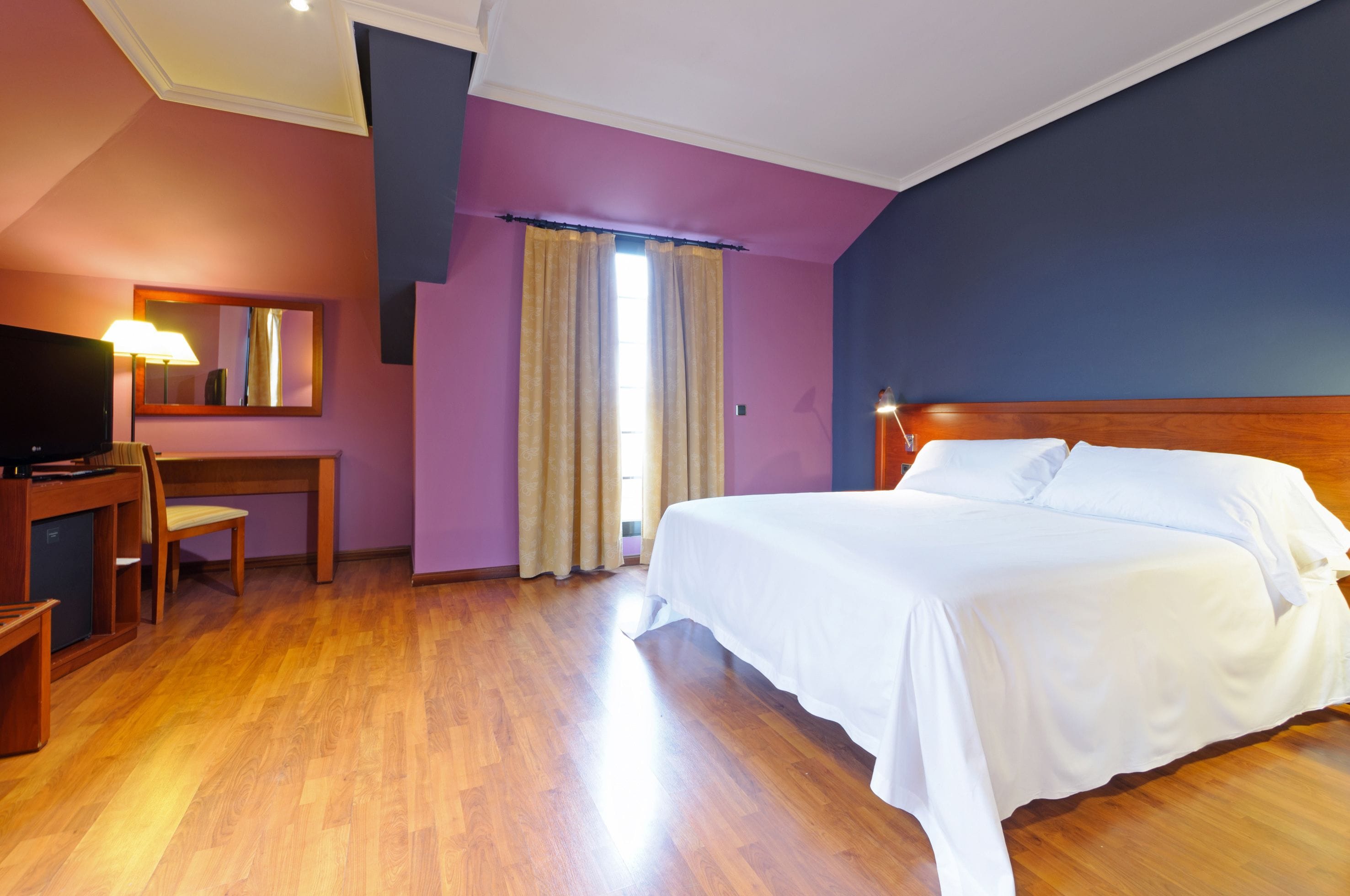 A hotel room with a wooden bed, a desk with a lamp, and a television.