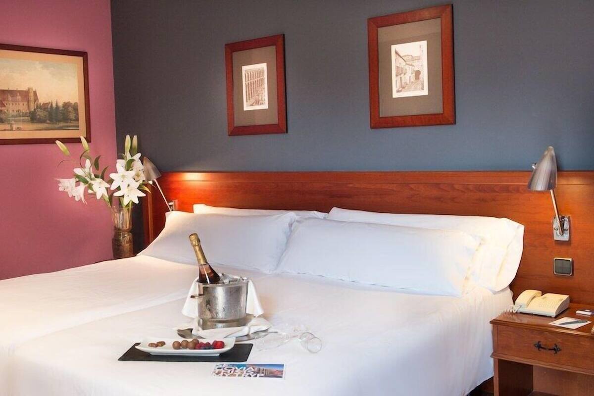A hotel room with a bed, a nightstand, a lamp, and framed pictures on the wall.