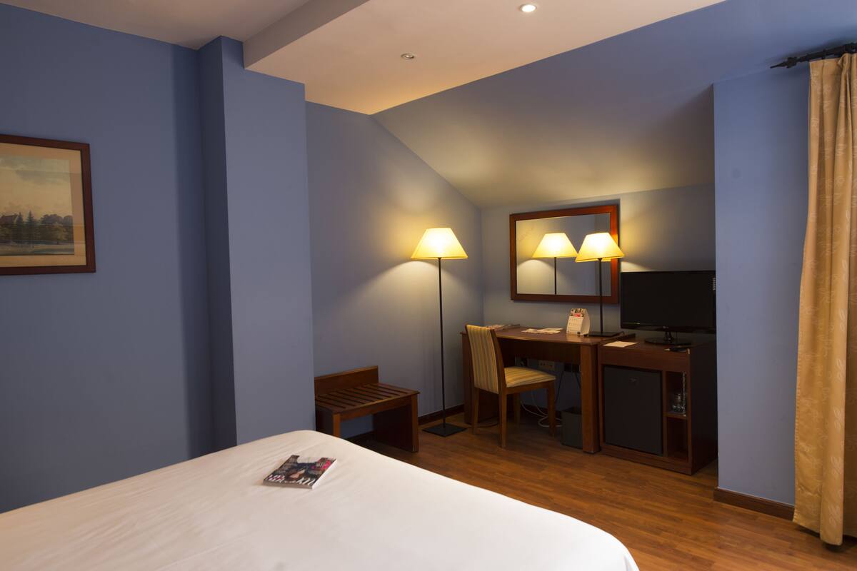 A hotel room with a bed, desk, chair, and a television.