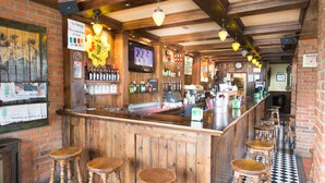 A bar with wooden bar stools, a brick wall, and a black and white checkered floor. - Hotel Segovia Sierra de Guadarrama (El Espinar)