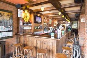 Un bar con taburetes de madera, una pared de ladrillo y un suelo a cuadros blanco y negro.