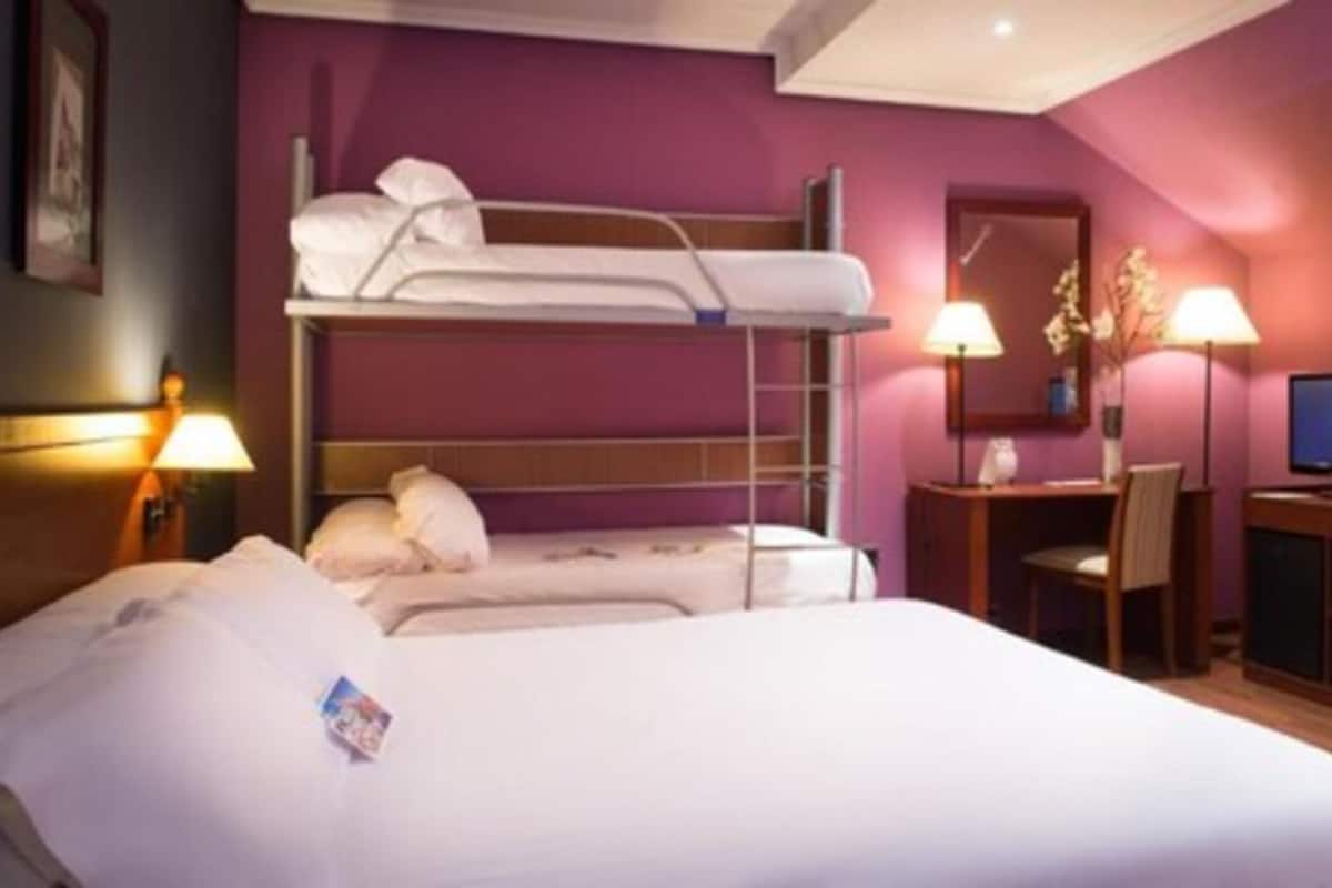 A hotel room with a bunk bed, a desk with a chair, a lamp, and a television.