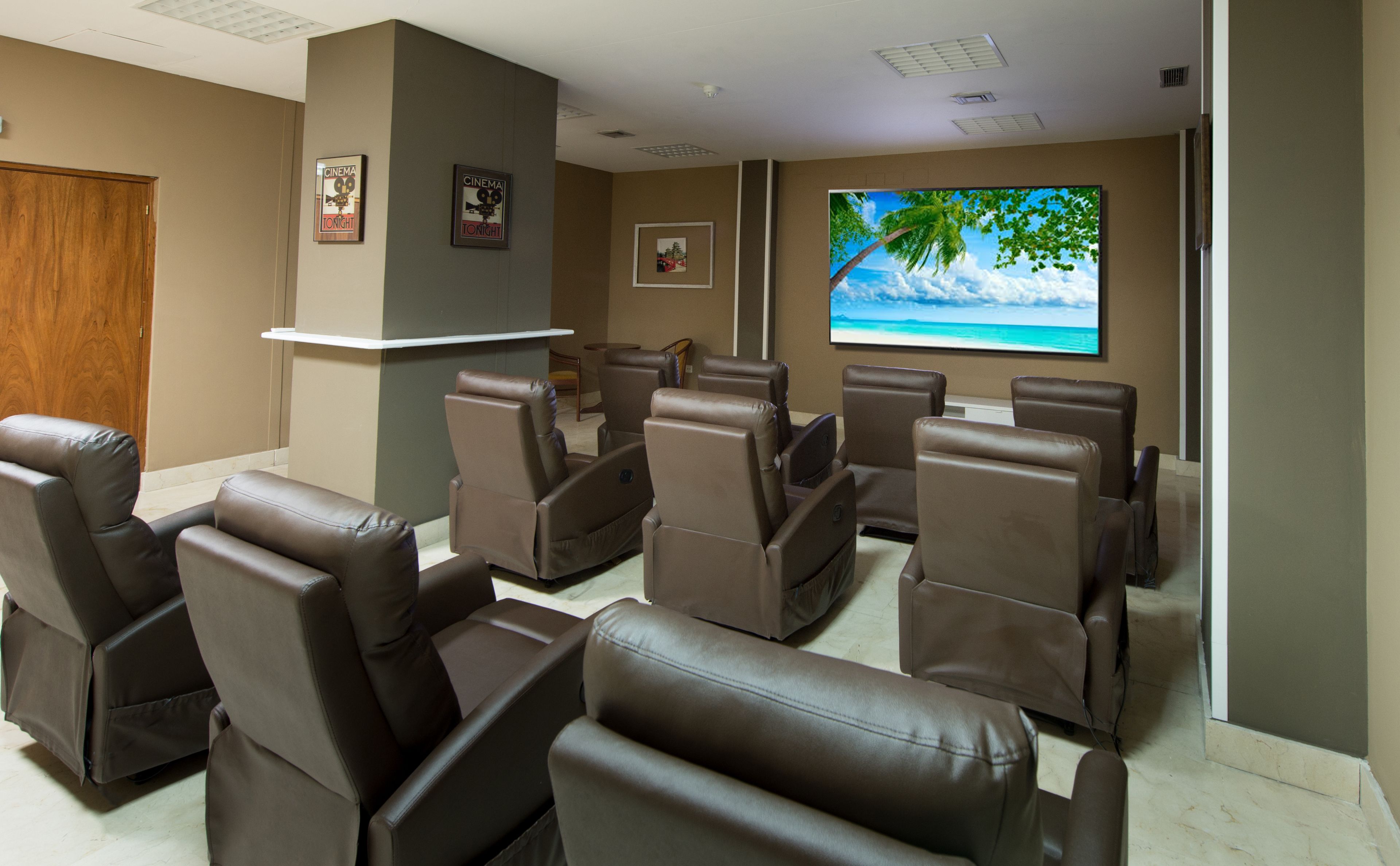Un cine en casa con varios sillones reclinables, una pantalla grande y cuadros en las paredes.
