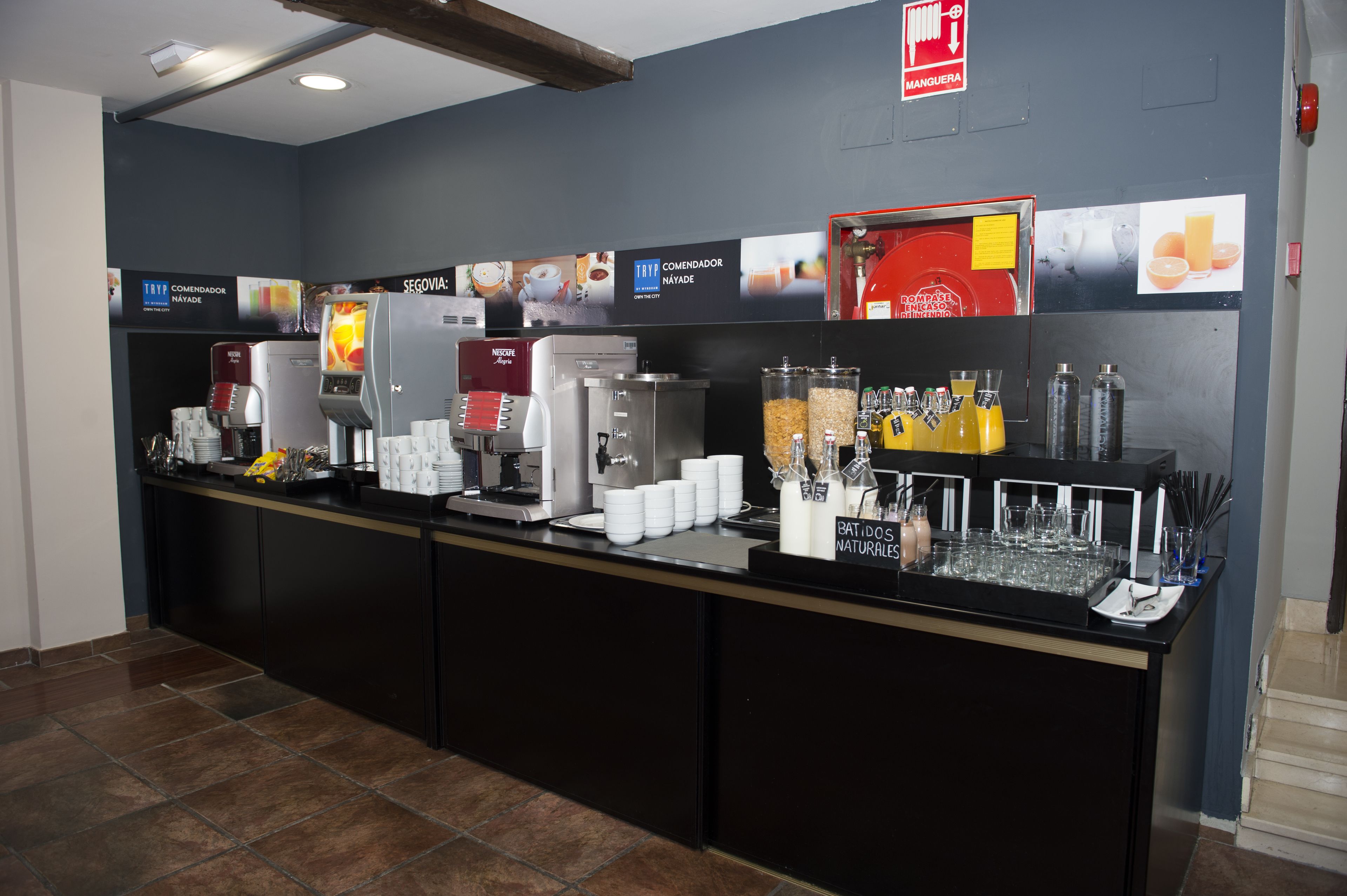A self-service beverage station with multiple coffee machines, a juice dispenser, and a variety of drink containers.