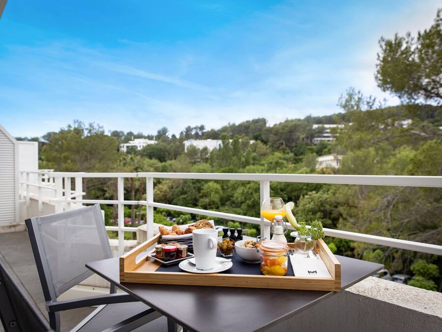 A breakfast tray on a balcony with a scenic view of trees and buildings.