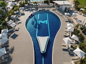 An aerial view of a resort with a large swimming pool, sun loungers, and umbrellas.