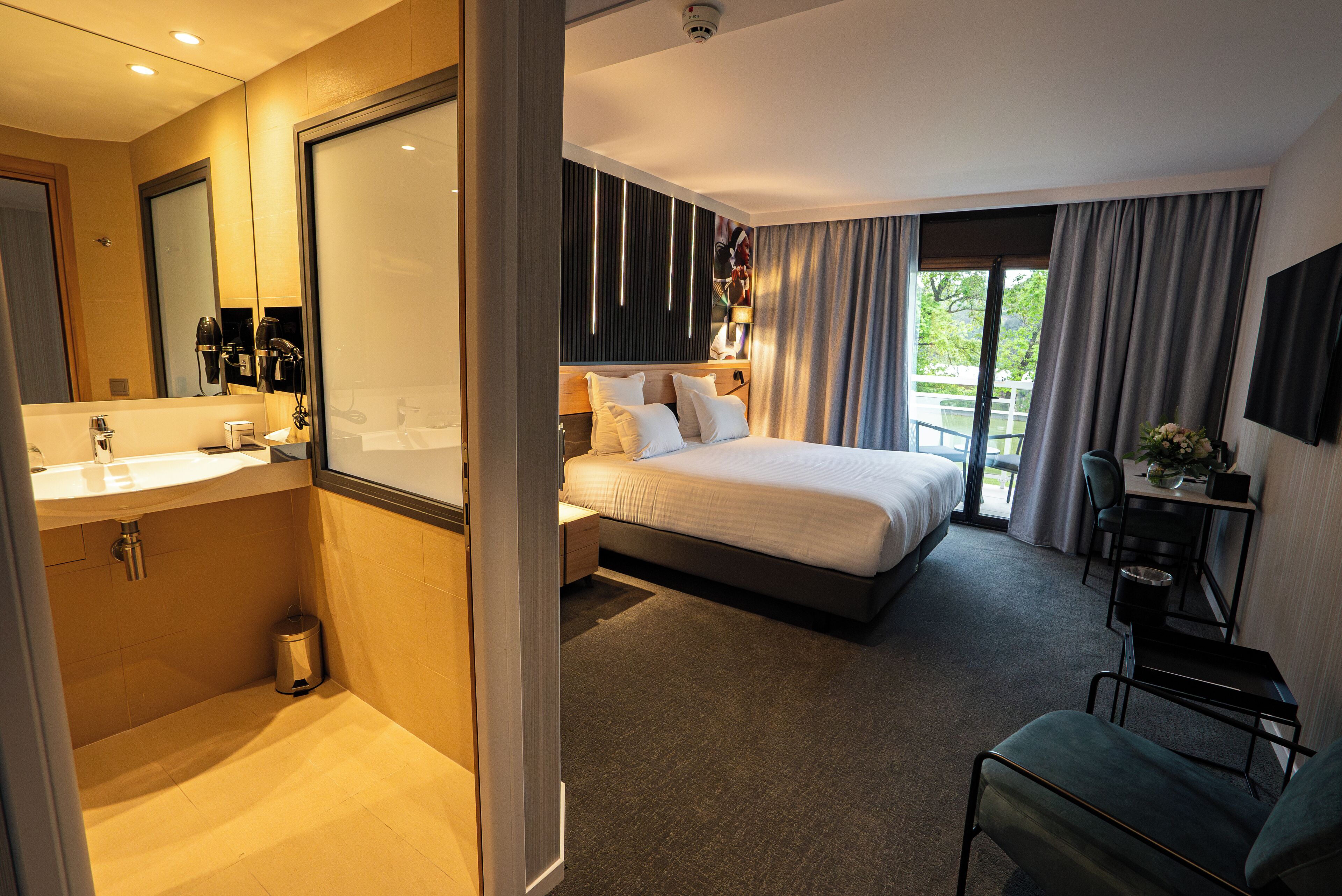 Habitación de hotel con una cama grande, un escritorio, una silla, un baño con lavamanos y un espejo.