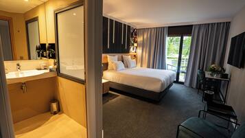 Habitación de hotel con una cama grande, un escritorio, una silla, un baño con lavamanos y un espejo.