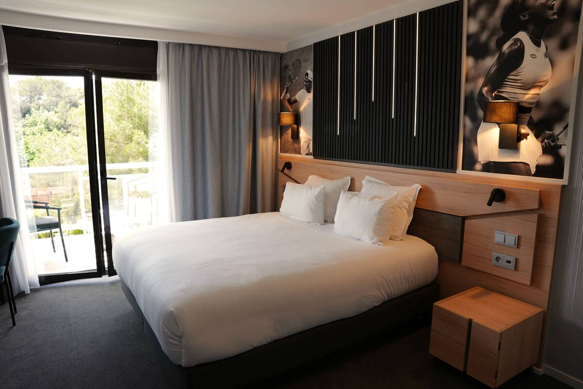 A modern hotel room with a large bed, a wooden nightstand, and a view of the outdoors.