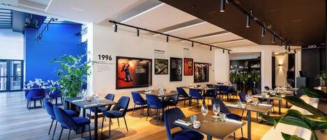 Un restaurant moderne avec des chaises bleues, des tables en bois et une grande plante.