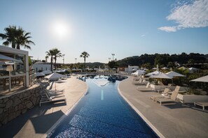 A swimming pool with lounge chairs and umbrellas, surrounded by palm trees and buildings. - Mouratoglou Hotel & Resort (Biot)