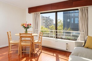 A modern apartment with a dining area, a sofa, a large window with a view of buildings, and a radiator. - MR Apart (Santiago)