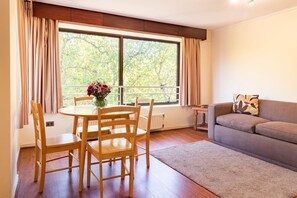 A room with a dining table, chairs, a sofa, a window with curtains, and a radiator. - MR Apart (Santiago)