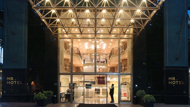A hotel entrance with a glass facade, a central staircase, and a geometric light structure above. - MR Apart (Santiago)