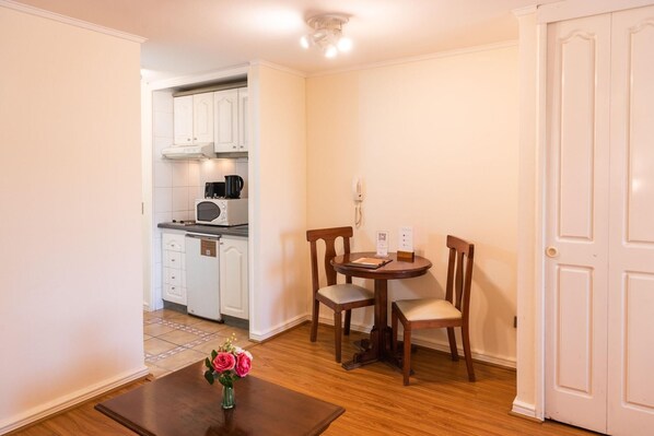 A compact kitchen with white cabinets, a microwave, and a coffee maker. There is a small dining table with two chairs and a vase with flowers. - MR Apart (Santiago)