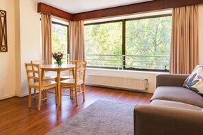 A room with a dining table, chairs, a radiator, a sofa, and large windows with curtains. - MR Apart (Santiago)