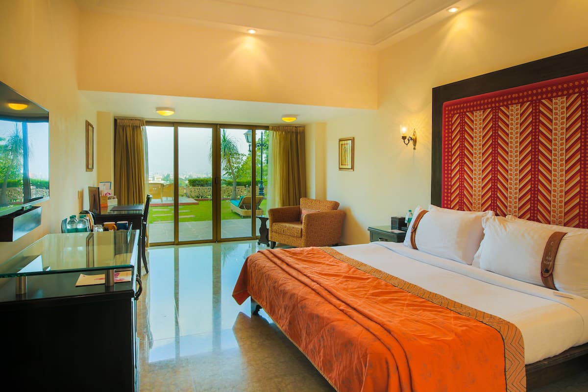 Une chambre d’hôtel avec un grand lit, un bureau, une chaise et une vue sur l’extérieur grâce à une porte coulissante.