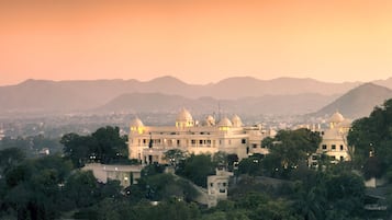 A large, multi-story building with domed structures, surrounded by lush greenery and mountains in the background.