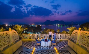 Una terraza con una mesa para dos, con vista a un lago y al paisaje urbano de noche.