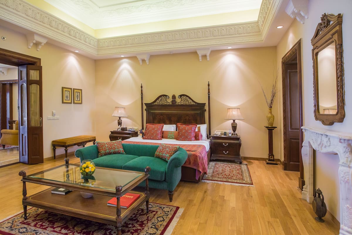 Une chambre spacieuse avec un grand lit, un canapé vert, une table basse en verre et une cheminée.
