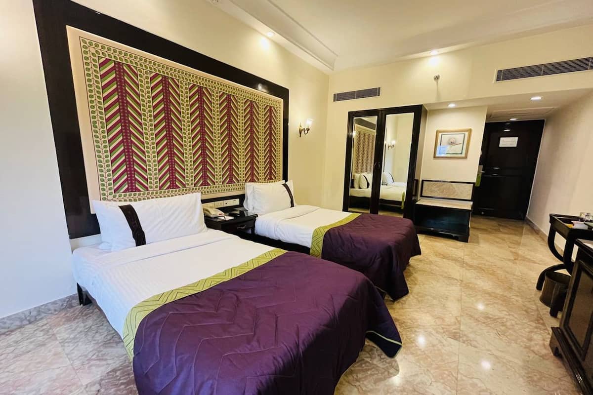 Une chambre d’hôtel avec deux lits, une grande tête de lit décorative, un bureau et un miroir.