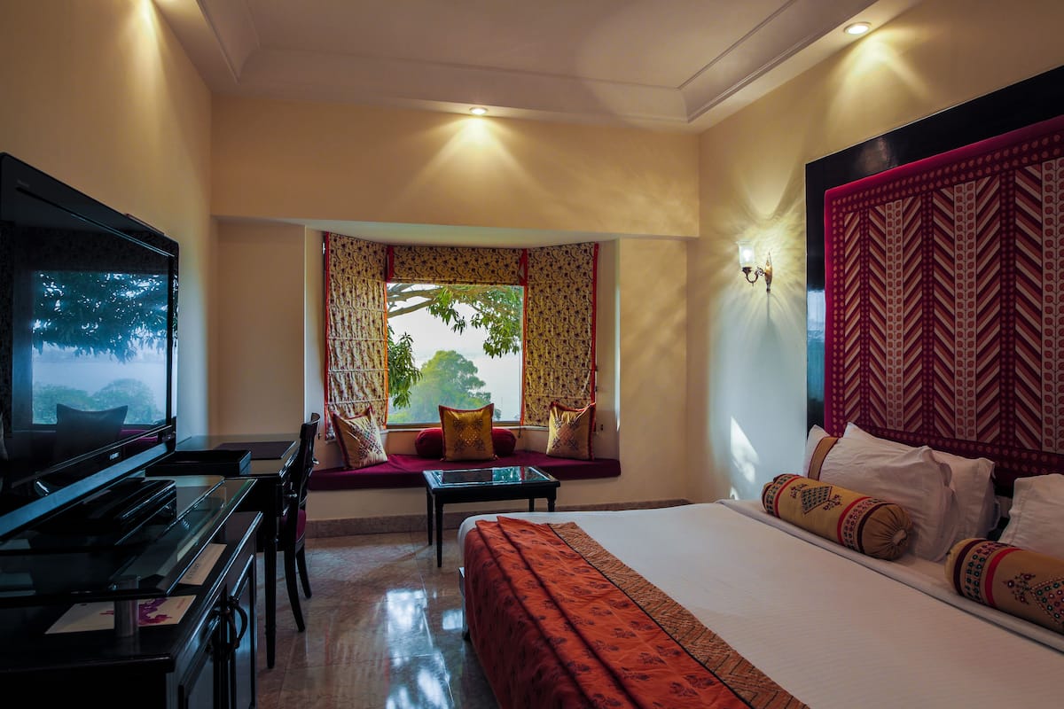 Une chambre d’hôtel avec un lit, une télévision, un piano, une fenêtre avec des rideaux et un lampadaire fixé au mur.