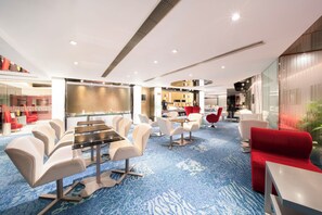 A modern hotel lobby with a blue carpet, white and red seating, and a kitchen area in the background. - Regal Oriental (Kowloon)
