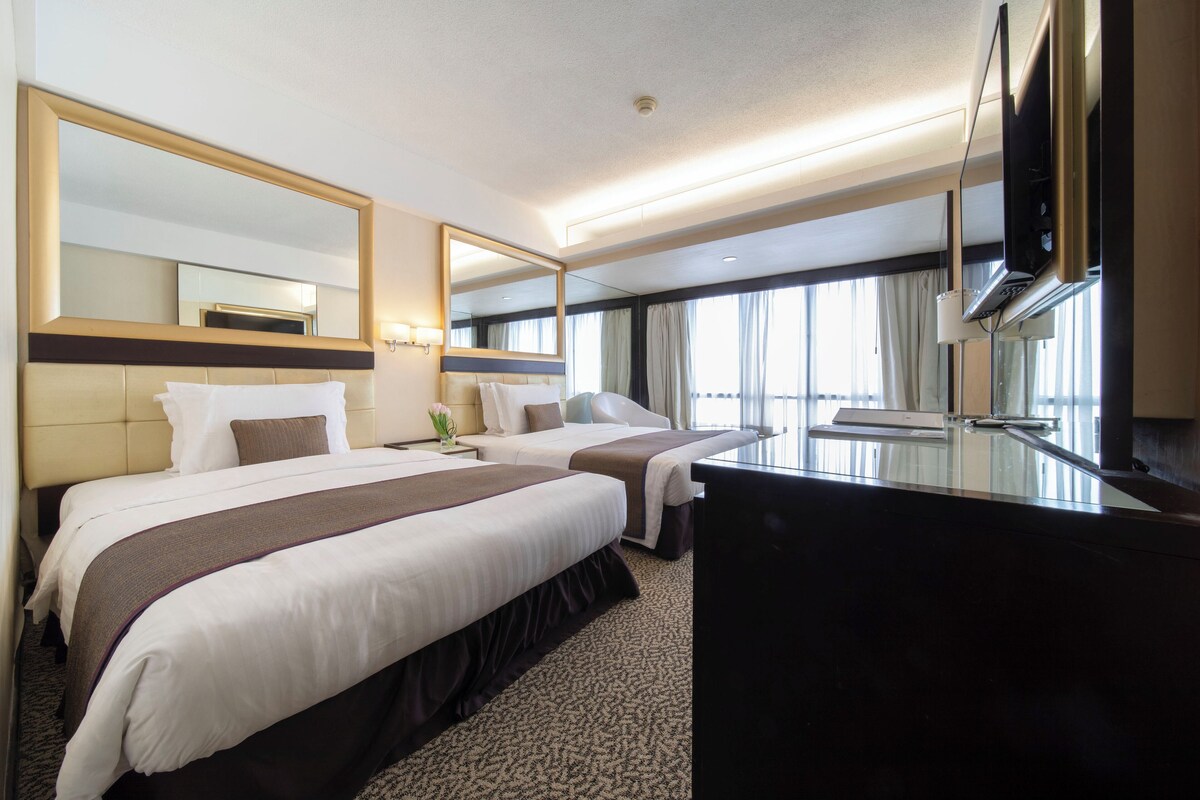A hotel room with two beds, a large mirror, a flat-screen TV, and a view of the outdoors.