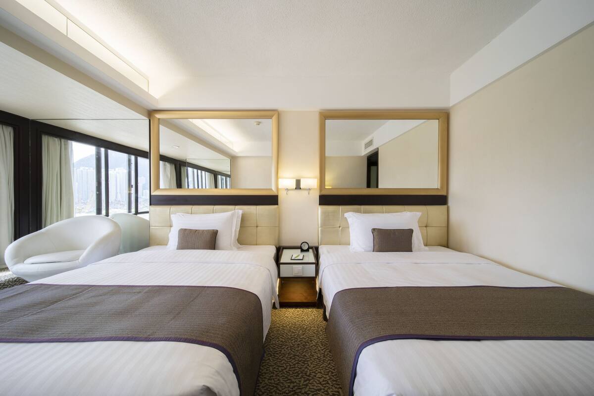 A hotel room with two beds, a chair, a nightstand with a lamp, and a large mirror.