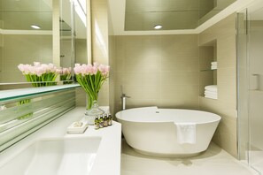 A modern bathroom with a freestanding bathtub, a glass shower enclosure, and a vanity with a mirror and a vase of flowers. - Regal Oriental (Kowloon)
