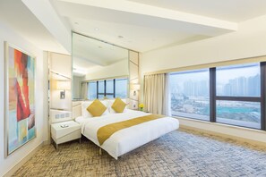 A modern hotel room with a large bed, a nightstand, a mirror, and a view of the city. - Regal Oriental (Kowloon)