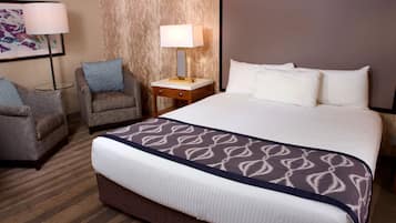 A hotel room with a large bed, two armchairs, a nightstand with a lamp, and a framed picture on the wall.