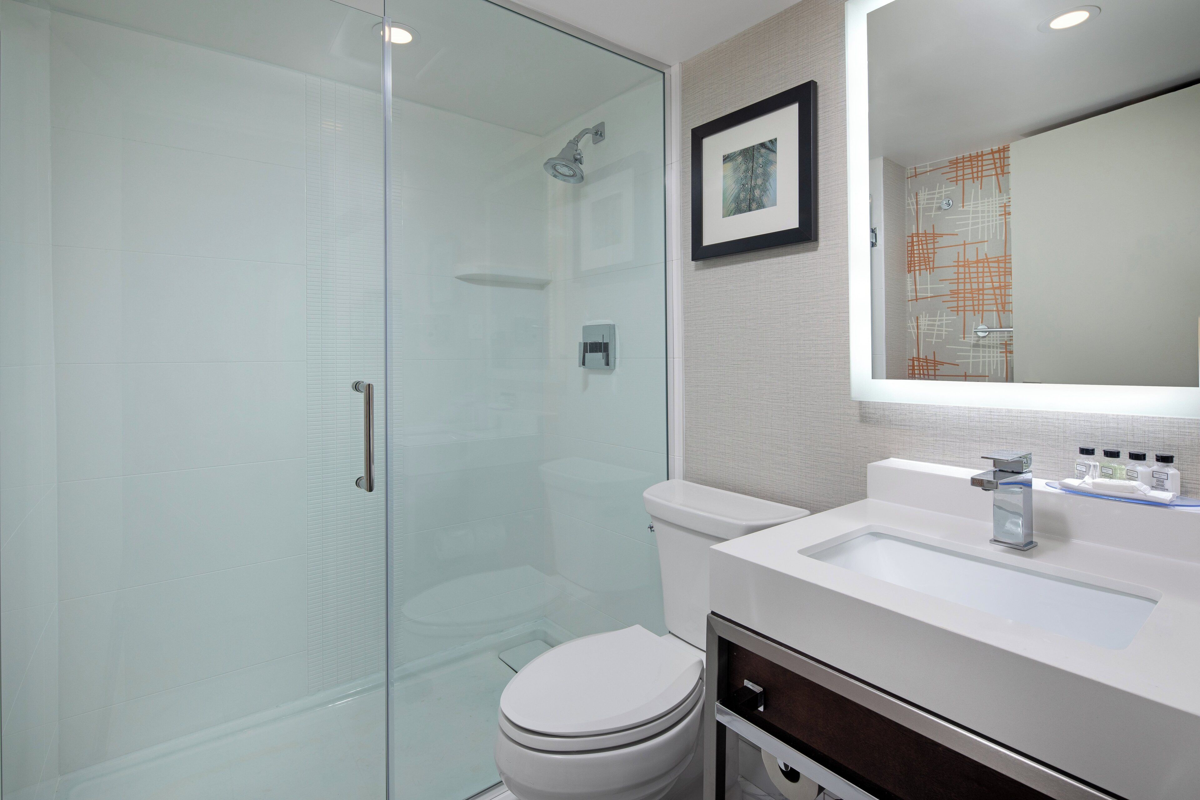 Un baño moderno con cabina de ducha de vidrio, inodoro blanco y lavabo con espejo arriba.