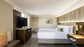 A hotel room with a large bed, a flat-screen TV, a desk, and a bench.