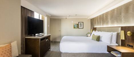 A hotel room with a large bed, a flat-screen TV, a desk, and a bench.