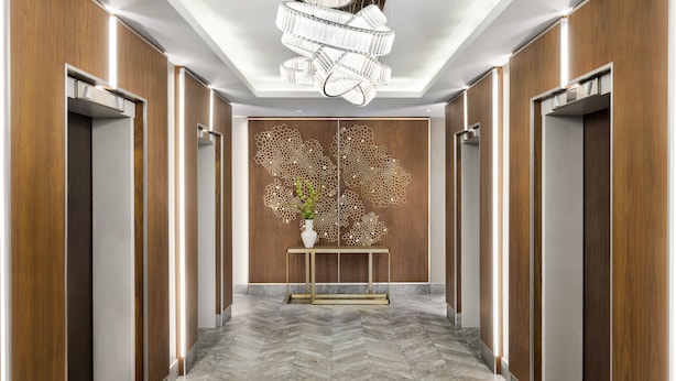 Un couloir moderne avec un lambris en bois, une console centrale agrémentée d’un vase et un luminaire au plafond au design original.