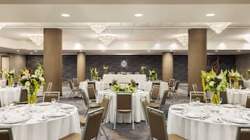 Un salón de banquetes con mesas redondas dispuestas para comer, grandes pilares y candelabros.