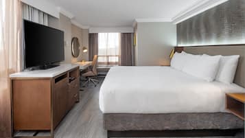 Habitación de hotel con una cama grande, un televisor de pantalla plana, un escritorio con una silla y un ventanal con cortinas.